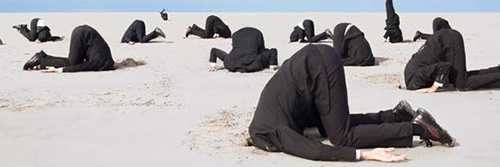 people in black suits on a beach with heads in the sand