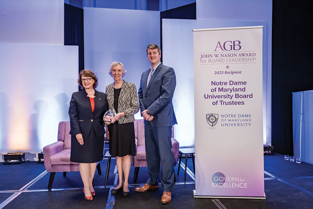 Three individuals stand together at an award ceremony. From left to right: Notre Dame of Maryland University President Marylou Yam wearing a navy suit with a red top, Patricia McLaughlin (board chair) in a black and white patterned jacket holding a crystal award, and Gregory FitzGerald (chief of staff and vice president for planning and external affairs) in a blue suit. They are positioned next to a banner reading 'AGB JOHN W. NASON AWARD for BOARD LEADERSHIP' and '2025 Recipient Notre Dame of Maryland University Board of Trustees' with the university's shield logo. Light purple chairs are visible in the background with blue lighting effects, and the banner displays 'GOVERN for EXCELLENCE' at the bottom.