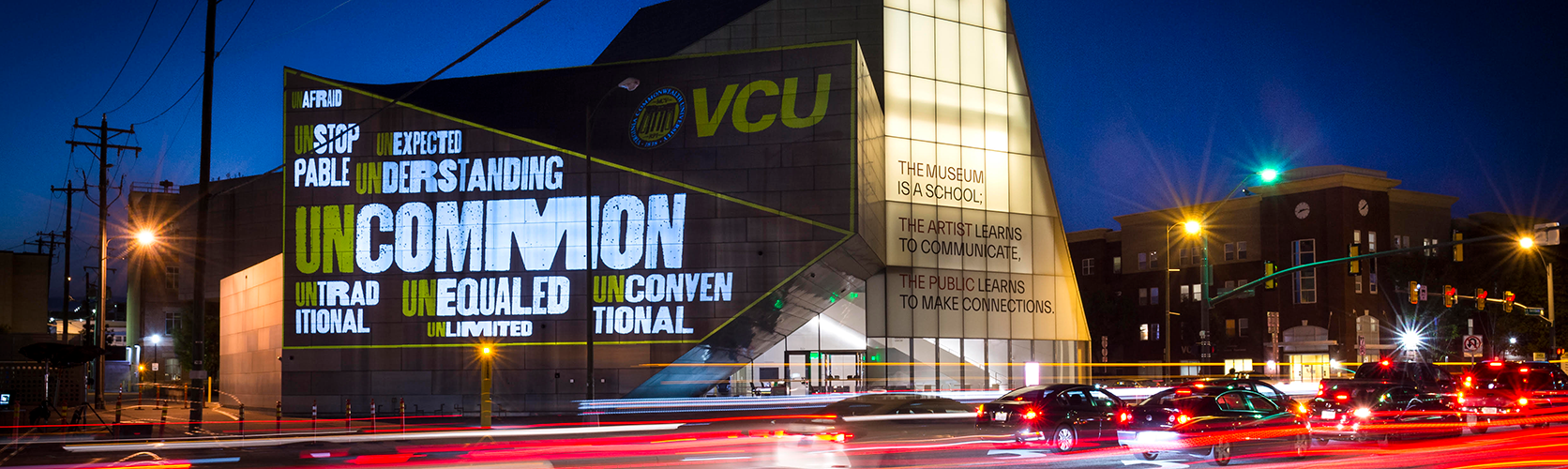 Nighttime view of the Institute for Contemporary Art’s Markel Center at Virginia Commonwealth University in Richmond, Virginia, with illuminated words, “UNCOMMON,” “UNEXPECTED,” “UNAFRAID,” “UNSTOPPABLE,” “UNDERSTANDING,” “UNTRADITIONAL,” “UNEQUALED,” “UNCONVENTIONAL,” and “UNLIMITED” projected on the building’s facade; car lights streak across the foreground.